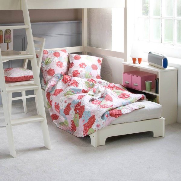 Unfolded futon in child's bedroom, with large window, desk and bookcase used as bedside table.