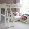 White bunk bed with corner desk and sleepover futon in a girl's bedroom, with a bookcase and large window.