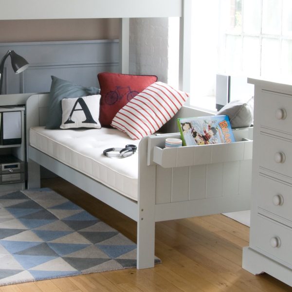 Close up of a child's day bed in light grey with a shelf on the end of the day bed.